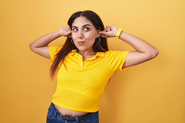 Young arab woman standing over yellow background smiling pulling ears with fingers, funny gesture. audition problem  - Photo, Image
