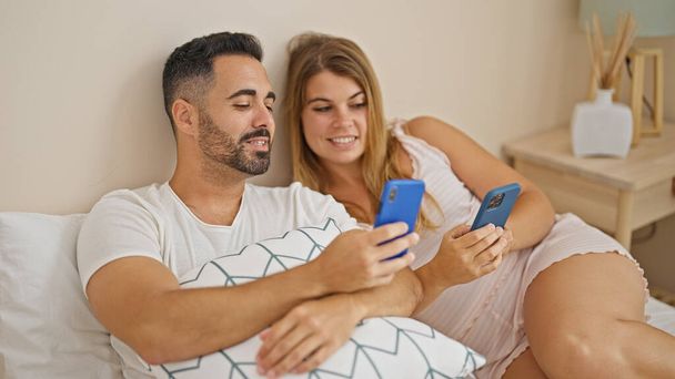 Homem e mulher casal sentado na cama usando smartphones falando no quarto - Foto, Imagem
