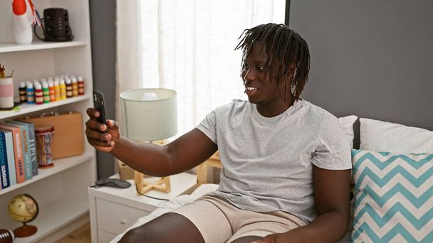 Afroamerikaner macht Videoanruf sitzend auf dem Bett im Schlafzimmer - Foto, Bild