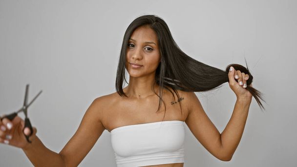 単離された白い背景をカットするためにハサミと髪を持っている若いラテン系女性 - 写真・画像