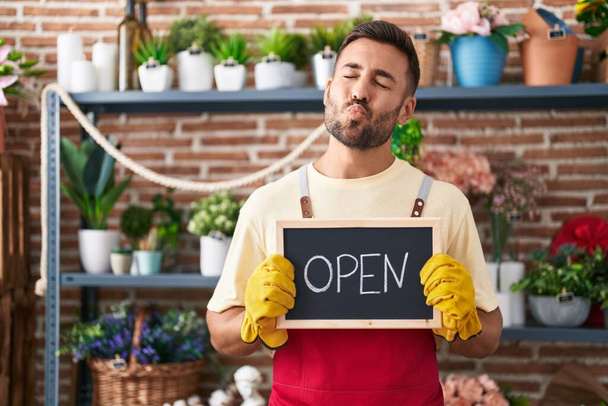 Handsome hispanic man working at florist holding open sign looking at the camera blowing a kiss being lovely and sexy. love expression.  - Photo, Image