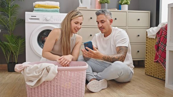 Mann und Frau waschen Wäsche mit Smartphone in Waschküche - Foto, Bild