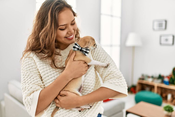 Young beautiful hispanic woman smiling confident hugging dog at home - 写真・画像