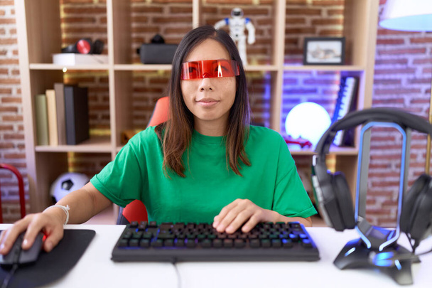 Chińska kobieta w średnim wieku w okularach wirtualnej rzeczywistości uśmiechnięta patrząc w bok i patrząc myśląc.  - Zdjęcie, obraz