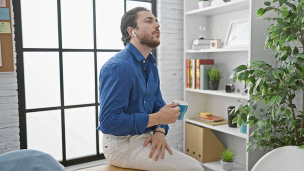 Trabajador de negocios hispano joven con auriculares bebiendo café en la oficina - Foto, Imagen