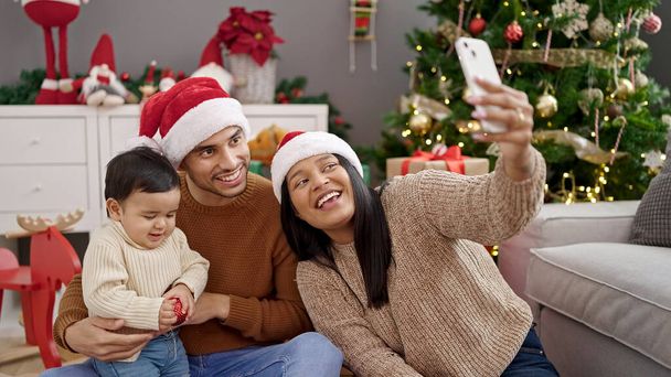 Ζευγάρι και γιος κάνουν selfie από smartphone κάθεται στο πάτωμα από χριστουγεννιάτικο δέντρο στο σπίτι - Φωτογραφία, εικόνα
