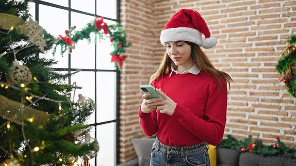Młoda latynoska kobieta świętuje Boże Narodzenie za pomocą smartfona w domu - Zdjęcie, obraz