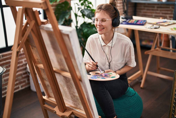 Joven mujer rubia artista escuchando música dibujo en el estudio de arte - Foto, Imagen