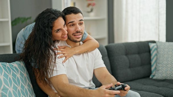 Άνδρες και γυναίκες ζευγάρι που παίζουν βιντεοπαιχνίδι καθισμένοι στον καναπέ στο σπίτι - Φωτογραφία, εικόνα