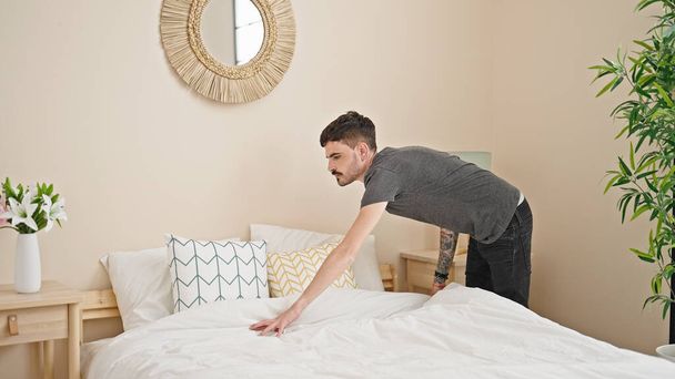 Young hispanic man make bed at bedroom - Фото, зображення