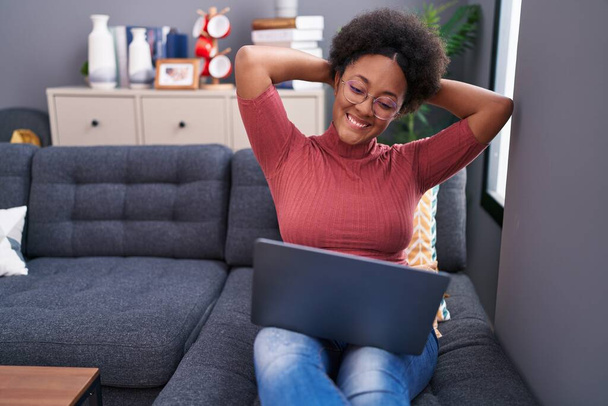African american woman using laptop relaxed with hands on head at home - Foto, Bild