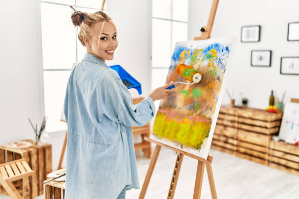 Young caucasian woman artist using paint roller drawing at art studio - Photo, Image