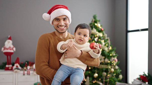 Ojciec i syn przytulają się do siebie świętując Boże Narodzenie stojąc w domu - Zdjęcie, obraz