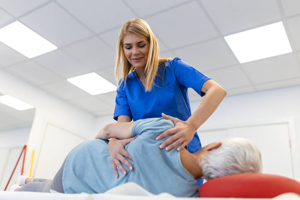 Orvos vagy fizioterapeuta segít meggyógyítani egy idős nő hátát. és tanácsokat ad a rehabilitációs központban. A fizikai rehabilitáció fogalma. - Fotó, kép