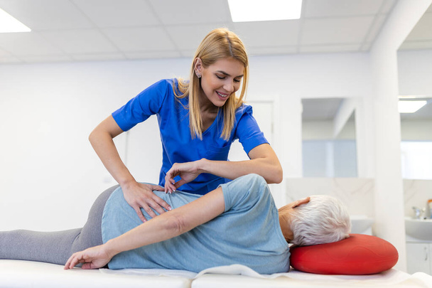 Fiatal orvos csontkovács vagy osteopath rögzíti hazug idős nő vissza kézmozdulatokkal látogatás közben a manuális terápiás klinikán. Szakmai csontkovács munka közben - Fotó, kép