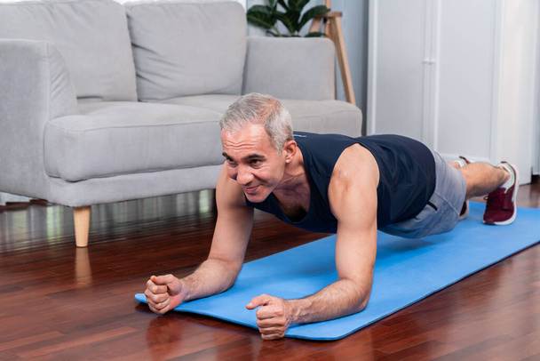 Urheilu ja urheilullinen vanhempi mies istutus kunto käyttäessään matto kotona liikunta käsitteenä terveen istuvuuden kehon elämäntapa eläkkeelle jäämisen jälkeen. Vaikutusvalta - Valokuva, kuva