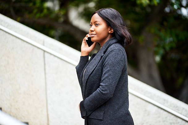 Jonge zwarte carrièrevrouw loopt buiten de trap op terwijl ze telefoneert. Hoge kwaliteit foto - Foto, afbeelding