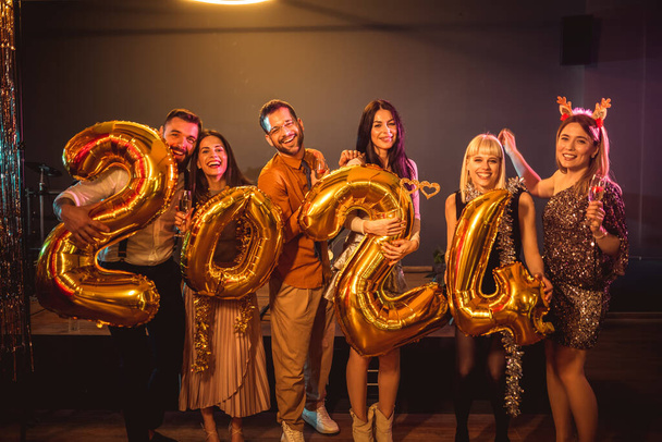 Eine Gruppe junger Leute feiert Neujahr im Nachtclub. Sie halten goldene Luftballons in der Hand - Foto, Bild