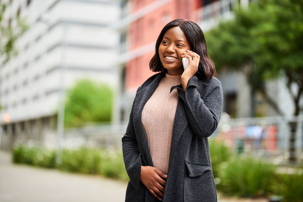 Egy fiatal fekete nő formális ruhában telefonál, miközben sétál kifelé. Kiváló minőségű fénykép - Fotó, kép