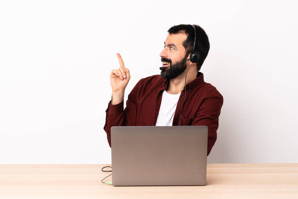Telemarketer valkoihoinen mies työskentelee kuulokkeiden ja kannettavan tietokoneen kanssa, joka aikoo toteuttaa ratkaisun nostaessaan sormea ylös. - Valokuva, kuva