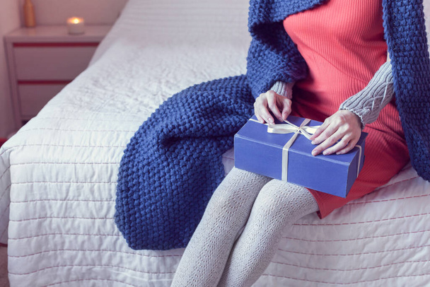chica en un vestido rojo abre un regalo mientras está sentado en la cama - Foto, Imagen
