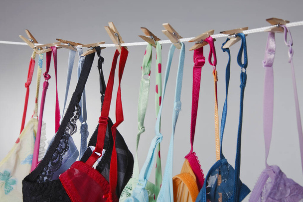 Um grupo de sutiãs coloridos pendurar em uma linha de roupas em um ambiente de estúdio - Foto, Imagem