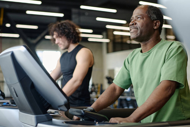 African american man walking on treadmill at gym with caucasian sportsman training on background - Photo, Image