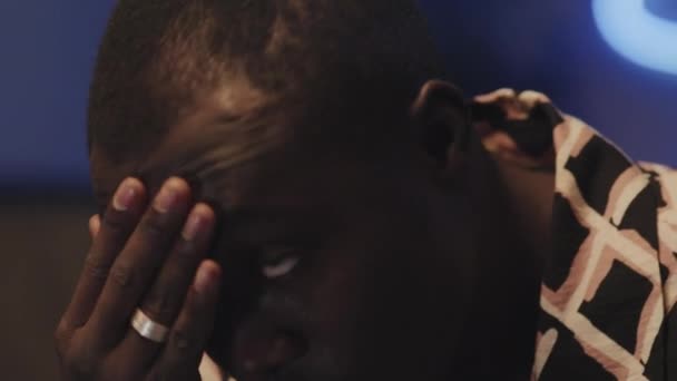 Закрыть снимок, на котором чернокожий парень плачет и вытирает слезы во время просмотра драмы, сериала или грустного видео по телевизору в помещении - Кадры, видео