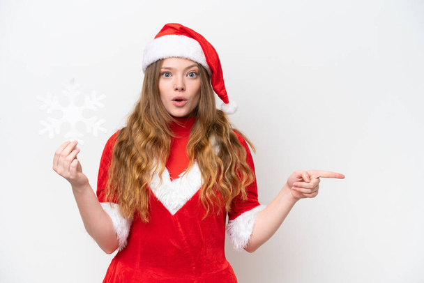 Young caucasian woman with Christmas dress holding snowflake isolated on white background surprised and pointing side - Photo, Image