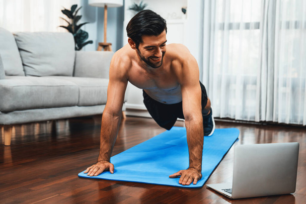 Atletyczny i sportowy mężczyzna robi pompki na macie fitness podczas sesji ćwiczeń online ciała dla sprawnego ciała i zdrowego stylu życia sportowego w domu. Gaiety domu ćwiczenia trening. - Zdjęcie, obraz