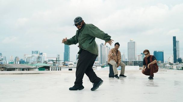 Professioneel breakdance team oefent B-boy dans terwijl multiculturele vrienden op het dak. Jonge moderne dansgroep die hiphop beweging doet. Stijl, mode, actie. Outdoor sport 2024. Inspannen.. - Foto, afbeelding