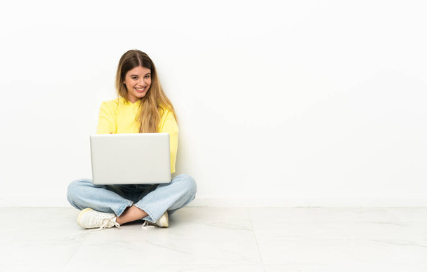 Młoda kobieta z laptopem siedząca na podłodze z skrzyżowanymi ramionami i patrząca w przyszłość - Zdjęcie, obraz