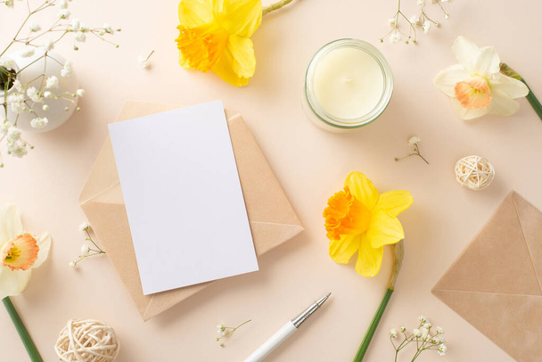 Send warm greetings for spring holidays with daffodils and gypsophila. Top view image showcases flowers, an envelope, and blank paper on a beige isolated background, perfect for adverts or text - Photo, Image
