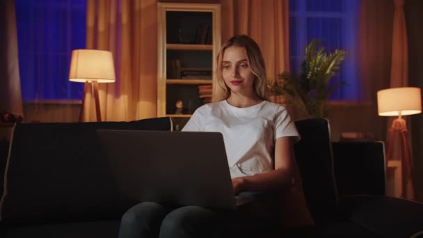Ένα ξανθό κορίτσι κάθεται στον καναπέ, περνά το βράδυ αναψυχής μετά την εργάσιμη ημέρα, χρησιμοποιεί ένα φορητό υπολογιστή για να διαβάσει ebook ή αντιστοιχεί με τους φίλους. Μια νεαρή επιχειρηματίας ελέγχει τη λειτουργία του ηλεκτρονικού καταστήματος της - Πλάνα, βίντεο