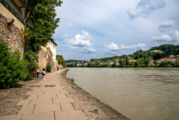 Passau, Lower Bavaria - DE  June 6, 2023 Horizontal view of Passaus picturesque walkway along the emerald green waters of the Inn River - Photo, Image