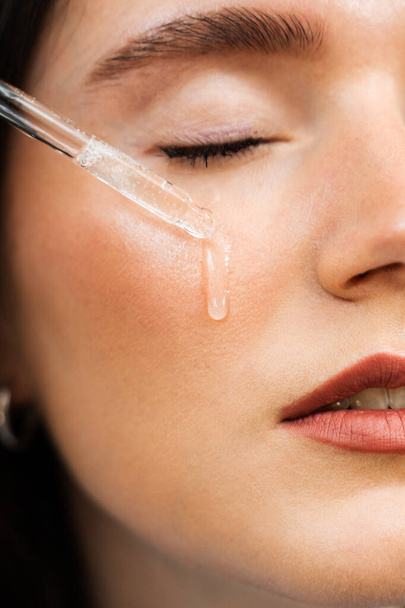 Aantrekkelijk meisje druppels etherische olie op gezichtshuid close-up. jonge vrouw is het aanbrengen van hydraterende serum op haar gezicht - Foto, afbeelding