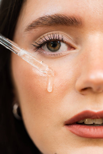 Young woman with acid dropper is applying drops of acid on her skin. Girl applying hyaluronic serum with pipette on face close-up - Φωτογραφία, εικόνα