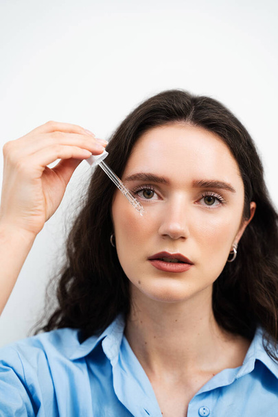 Girl is applying hyaluronic serum with pipette on face. Young woman with acid dropper is applying drops of acid on her skin - Photo, Image