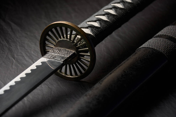 Foto horizontal de katana desenvainada con detalles de la empuñadura y la vaina, espada japonesa tradicional aislada sobre fondo negro. - Foto, Imagen