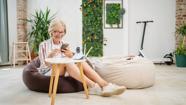 Yksi kypsä valkoihoinen nainen tilalla kotiin moderni turvallisuus valvontakamera ja matkapuhelin yrittää asentaa ja säätää yhteyden sovelluksen kopiotilaa - Valokuva, kuva