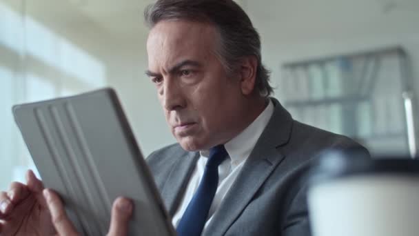 Primer plano medio del empresario anciano leyendo un nuevo plan de negocio mientras trabaja en la tableta digital en la oficina - Metraje, vídeo