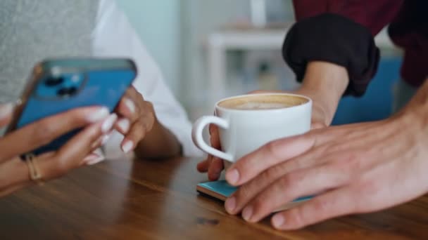 Barista hands putting cup delicious coffee on wooden table to woman client sitting with smartphone closeup. Unknown waiter bringing aromatic latte to african american girl. Young lady taking white mug - Footage, Video