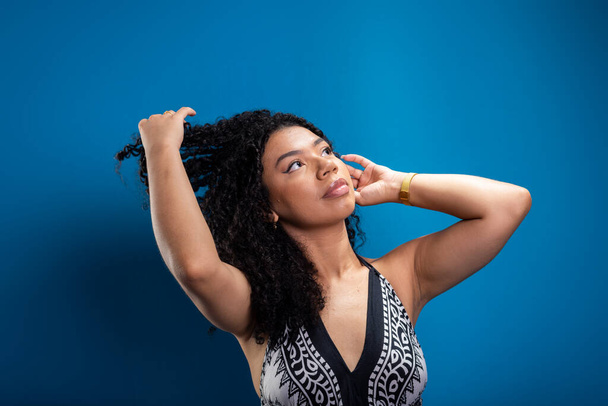 Portrait of beautiful woman touching her curly hair. Isolated on blue background. - Photo, Image