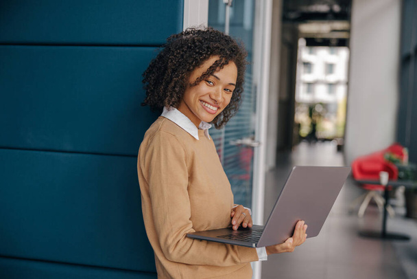 Hübsche Freelancerin arbeitet am Laptop, während sie auf modernem Coworking-Hintergrund steht - Foto, Bild