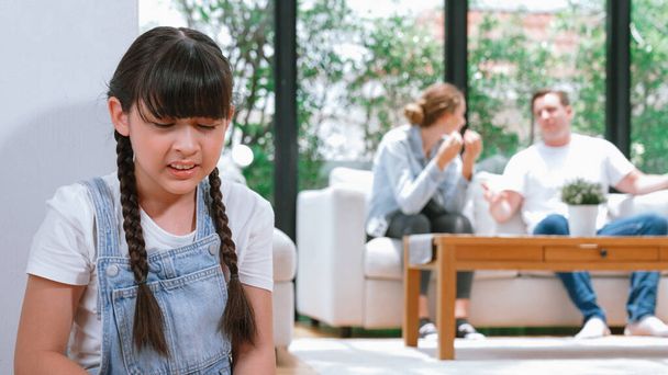 Stressed and unhappy young girl huddle in corner, cover her ears blocking sound of her parent arguing in background. Domestic violence at home and traumatic childhood develop to depression. Synchronos - Photo, Image