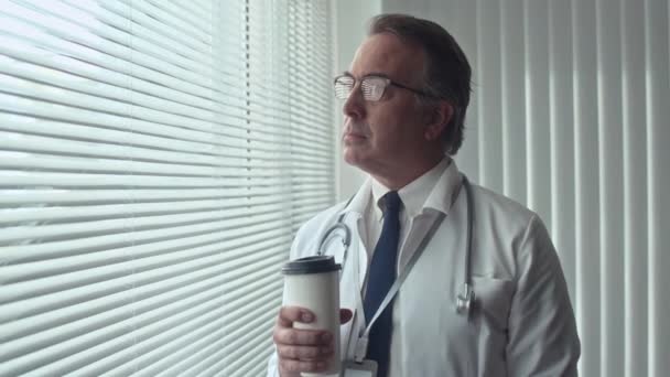 Retrato medio de médico general alegre tomando café y mirando a la cámara en el interior - Metraje, vídeo