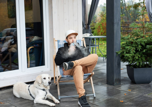 Young man sitting with golden retriever on terrace - Photo, Image