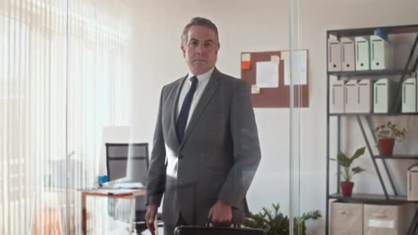 Kafkas CEO 'sunun evrak çantasını tutarken ve ofisteki kameraya bakarken orta uzunlukta portre fotoğrafı. - Video, Çekim