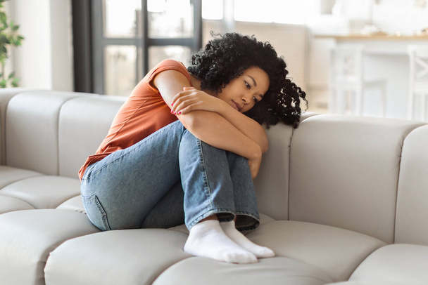 Porträt einer depressiven schwarzen Frau, die zu Hause auf der Couch sitzt, aufgebrachte Afroamerikanerin, die unter Apathie leidet, gebrochene Dame, die sich einsam und traurig fühlt, während sie sich auf dem Sofa ausruht, Kopierraum - Foto, Bild