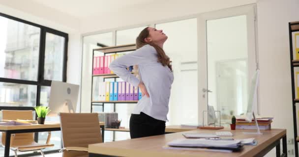 Mujer sostiene con la espalda con dolor de posición sentada incorrecta en el lugar de trabajo en la oficina de la empresa. Problemas de salud física y curvatura espinal - Metraje, vídeo